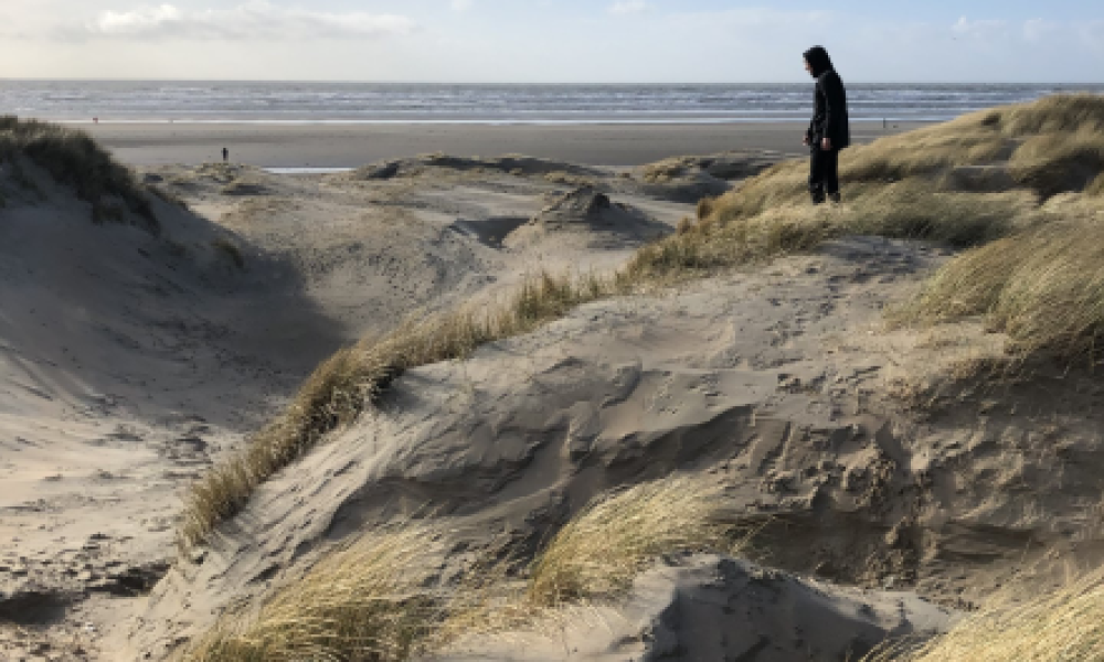 Persoon in de duinen met de zee op de achtergrond